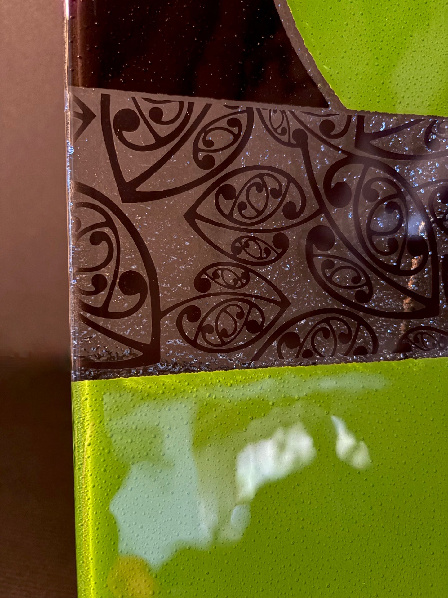close up of green and black rectangular fused glass plate showing maori kowhaiwhai pattern on a dark background