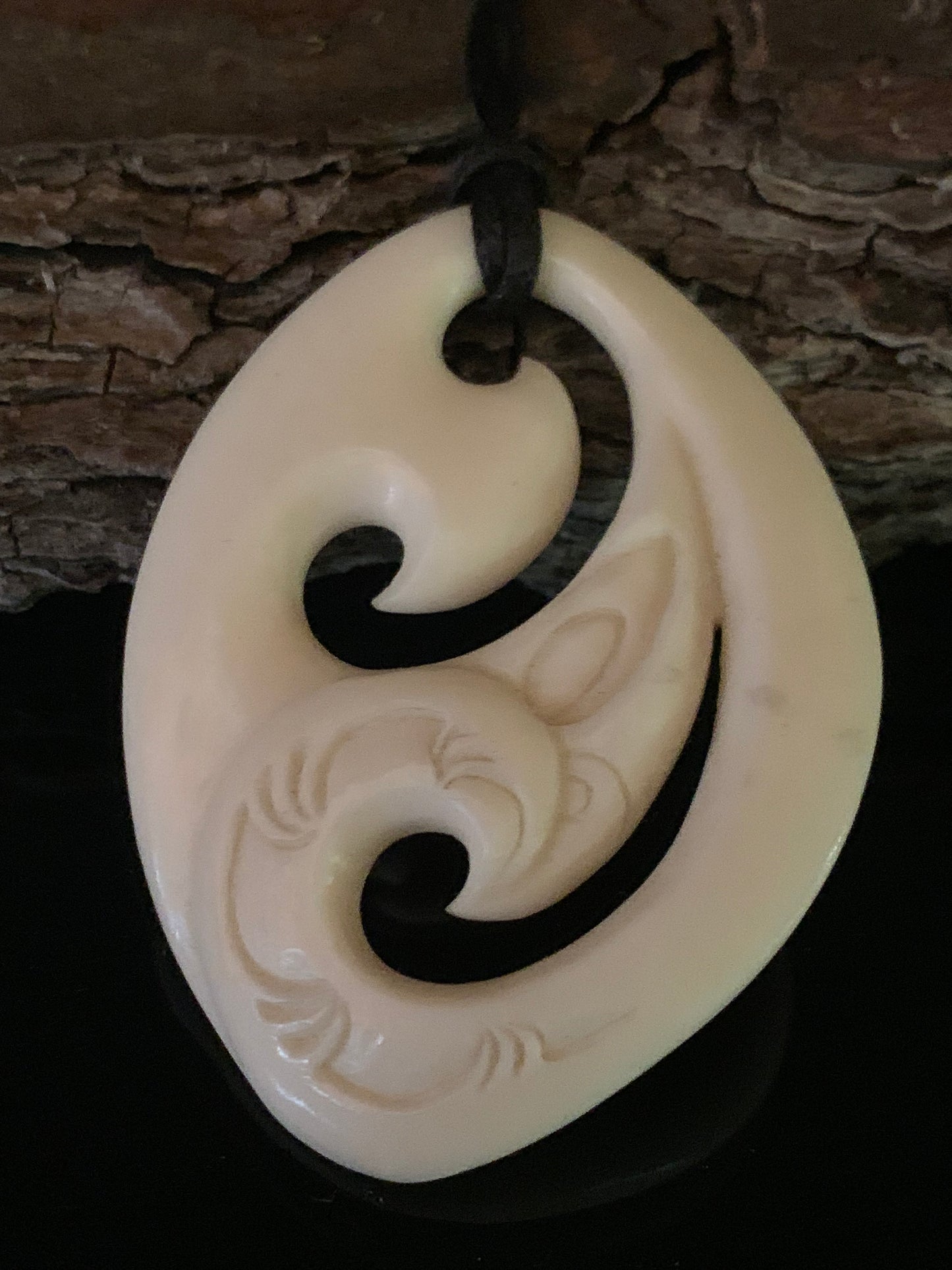 A bone pendant with Maori carvings, hanging on a waxed nylon cord against a wooden background.