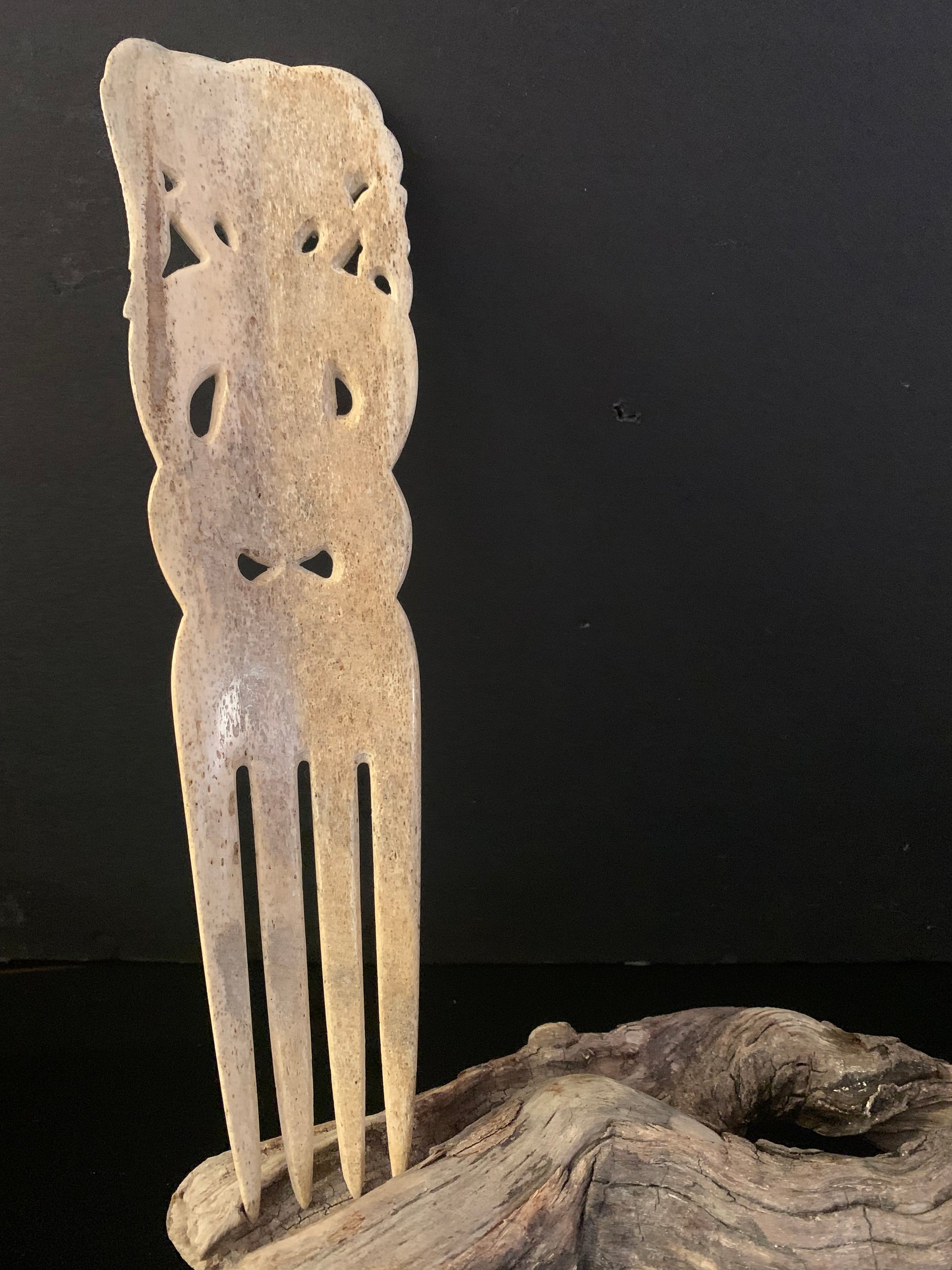 reverse side of a hand-carved whale bone comb with intricate designs and decorative elements, displayed on a wooden stand against a black background.