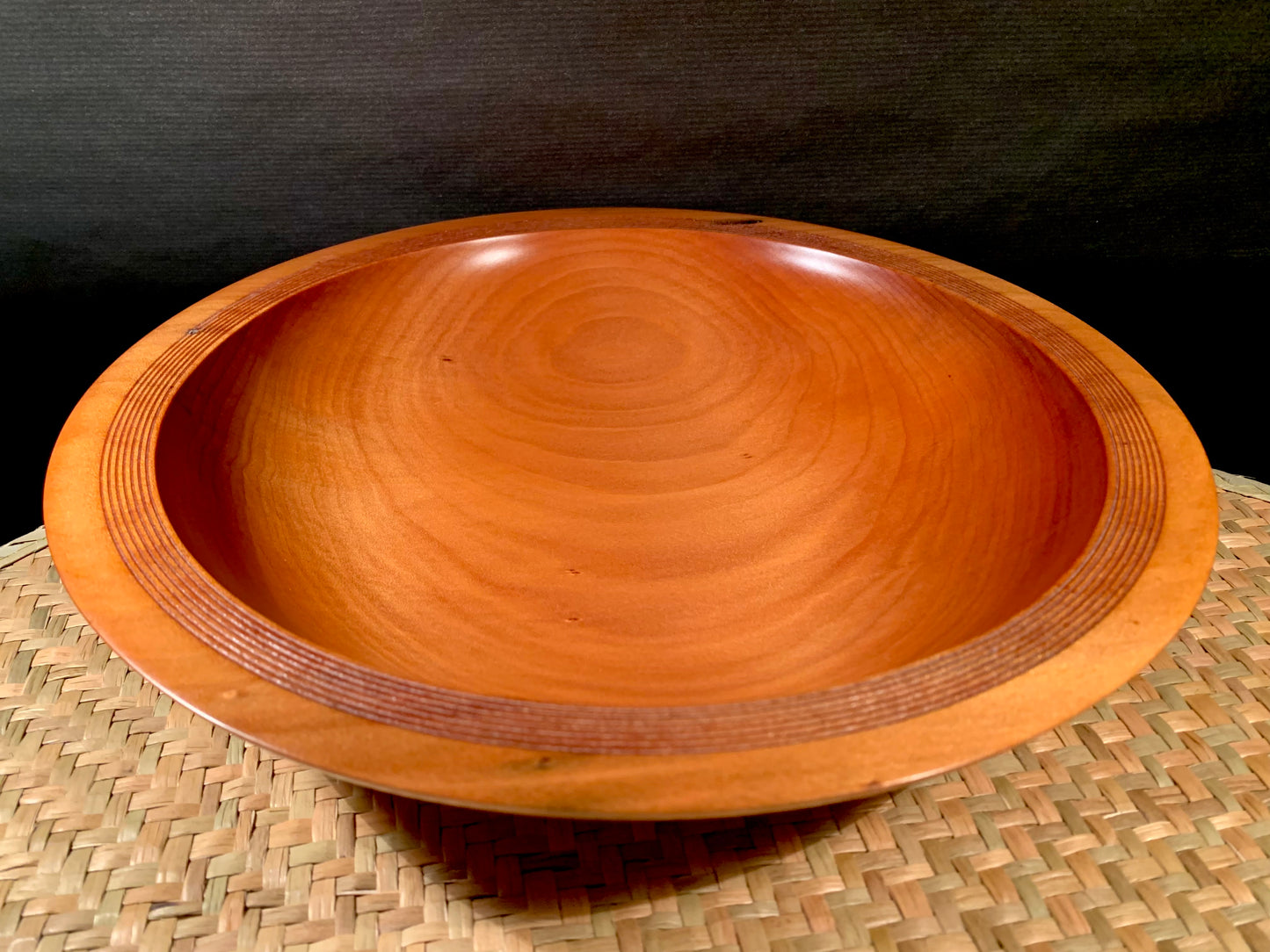 Woodturned bowl on a woven surface with a dark background.