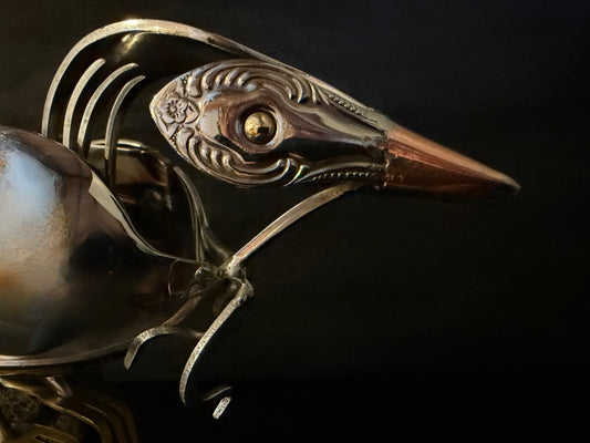showing headshot closeup of NZ tui bird head cutlery sculpture on a dark background
