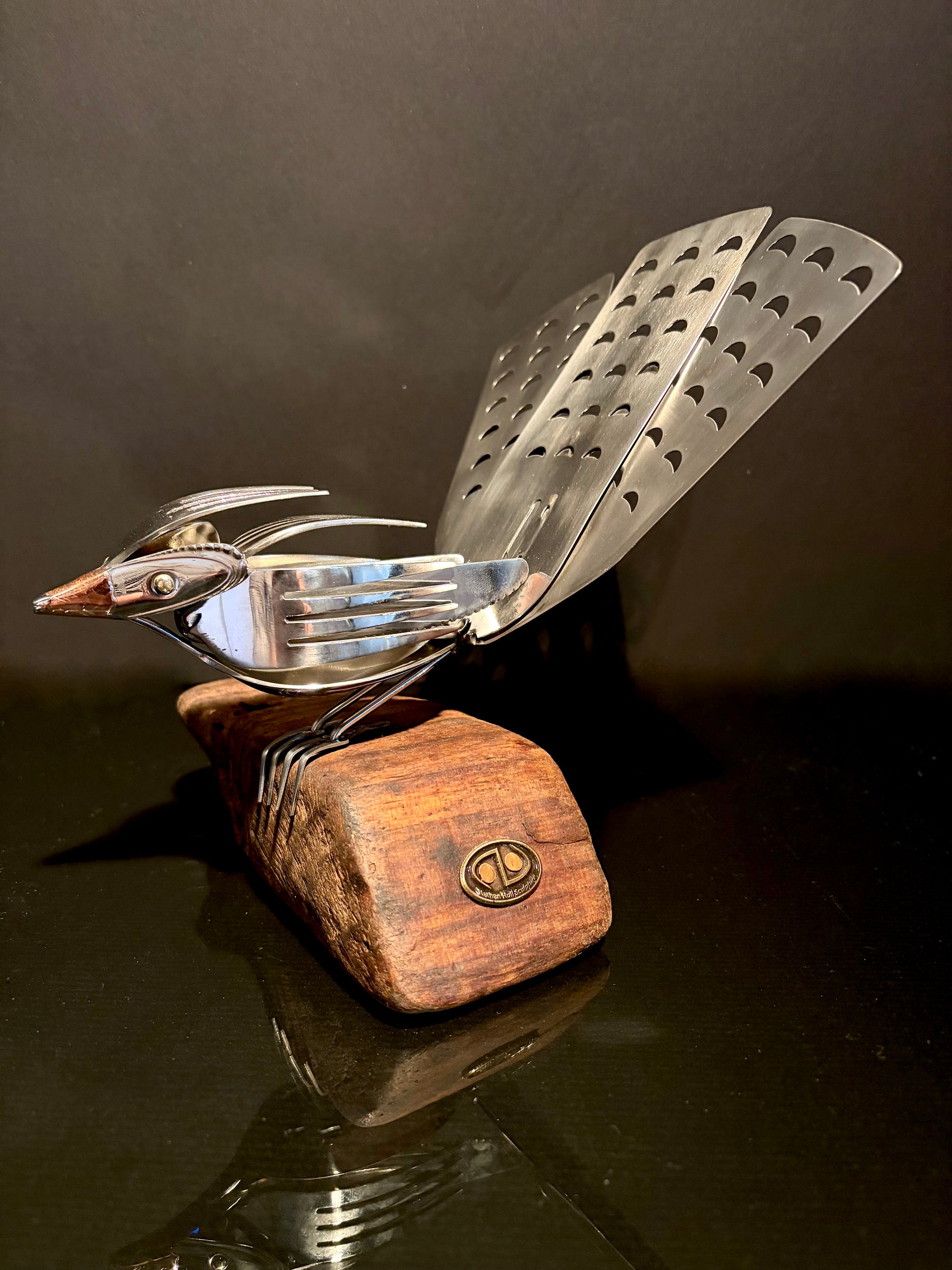 Metal bird sculpture with wooden base on a dark surface.