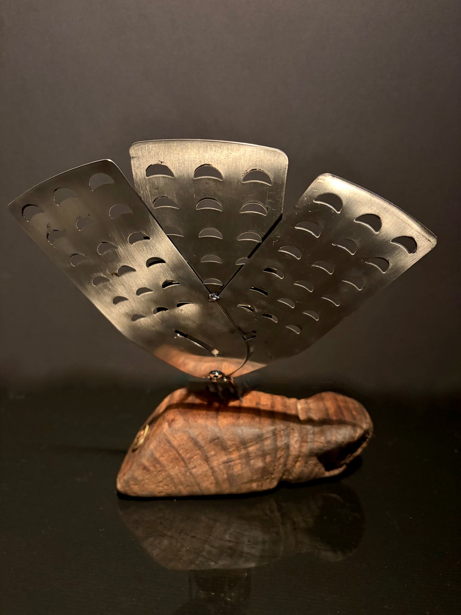 Decorative metal sculpture with a wooden base on a reflective surface.