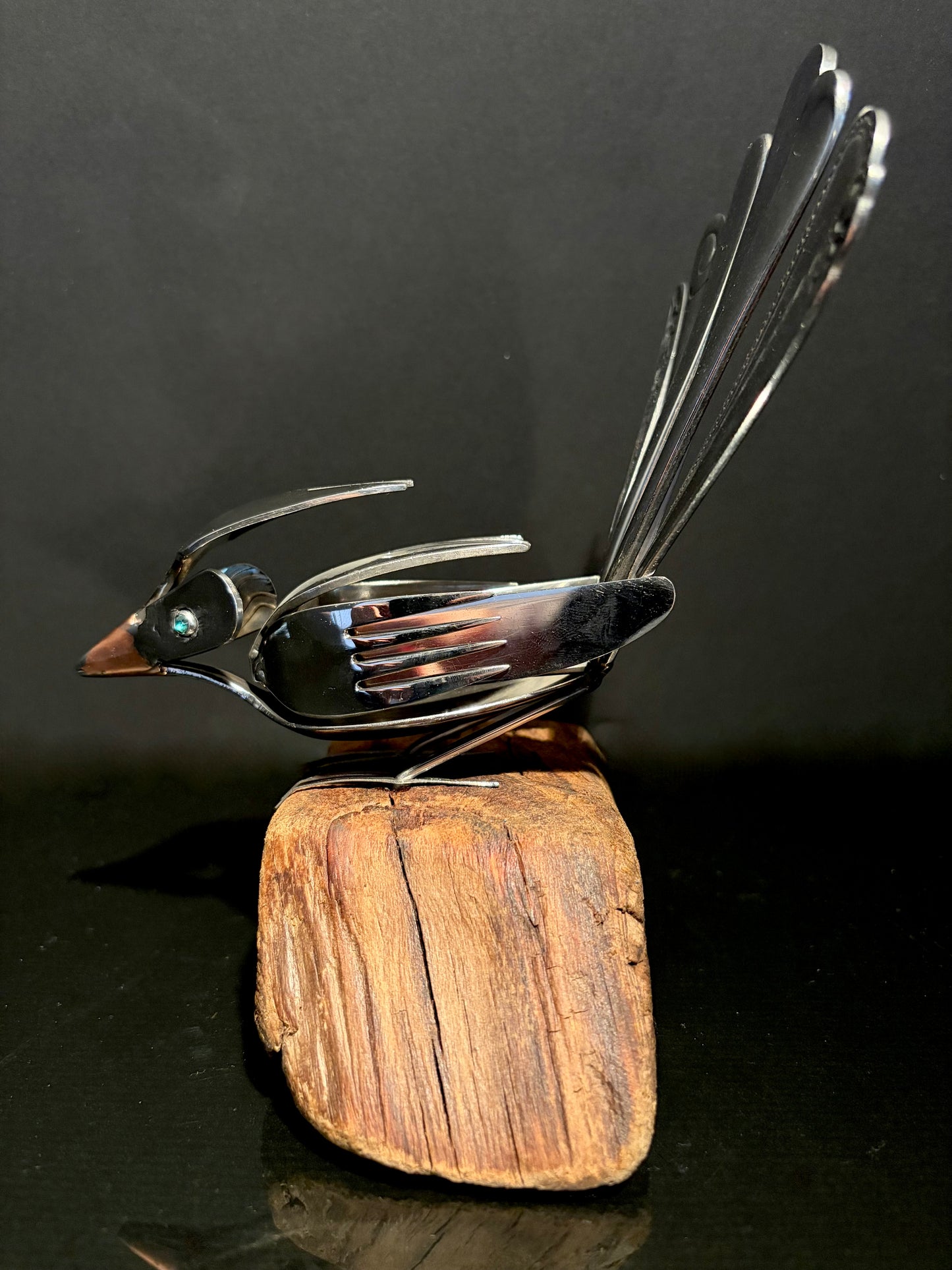 Spoon art sculpture of a bird perched on a wooden block.