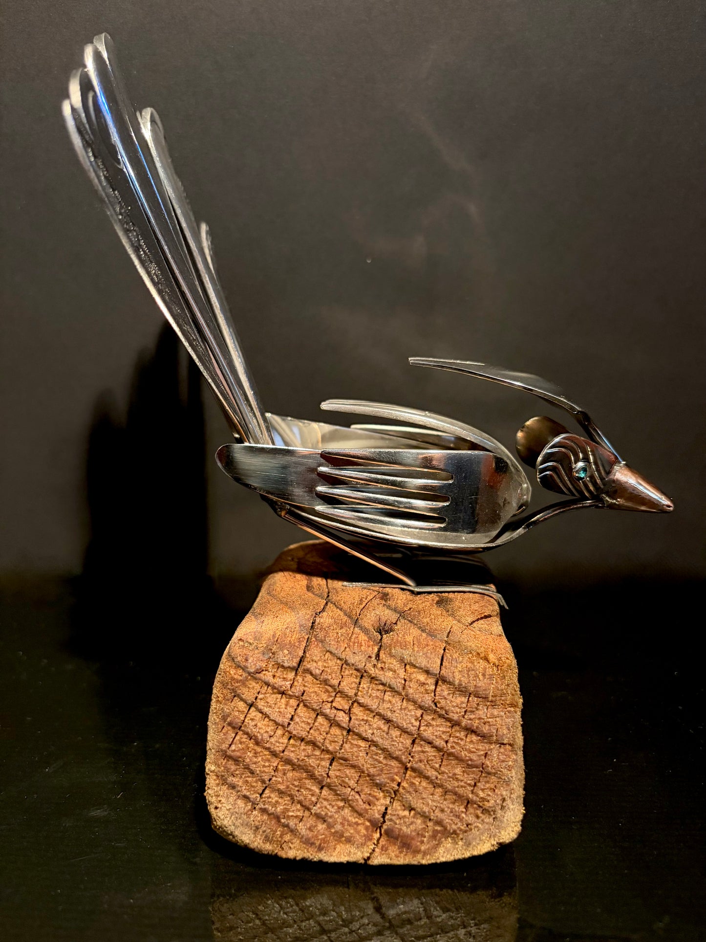 Metallic bird sculpture made from cutlery on a wooden base.
