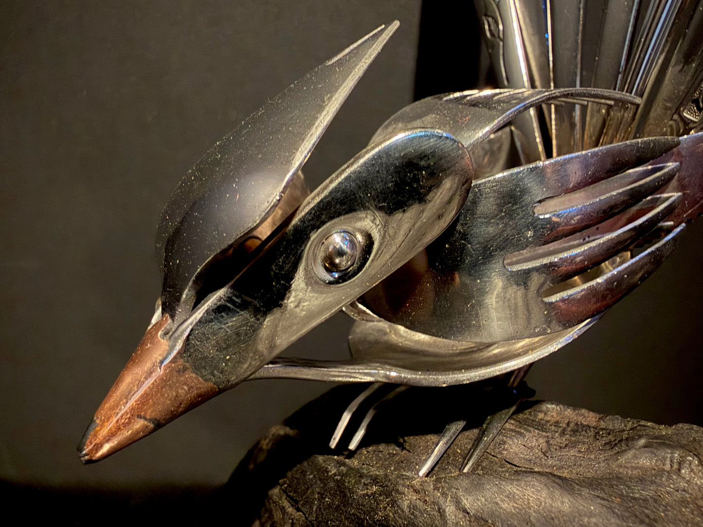 Metallic bird sculpture with a dark background.