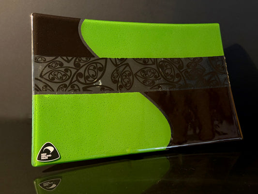 angled view of green and black rectangular fused glass plate with maori kowhaiwhai pattern on a dark background