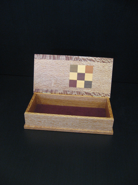 A small open wooden keepsake box with a hinged lid, featuring a decorative multicolor checkerboard inlay on the inside of the lid and a dark burgundy velvet lining.