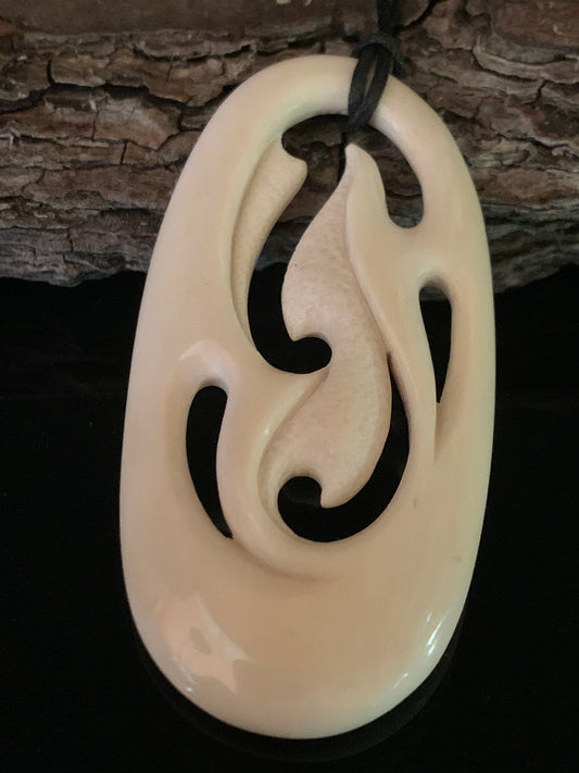 A bone freeform pendant with traditional Maori carvings, suspended on a waxed nylon cord against a wooden background.