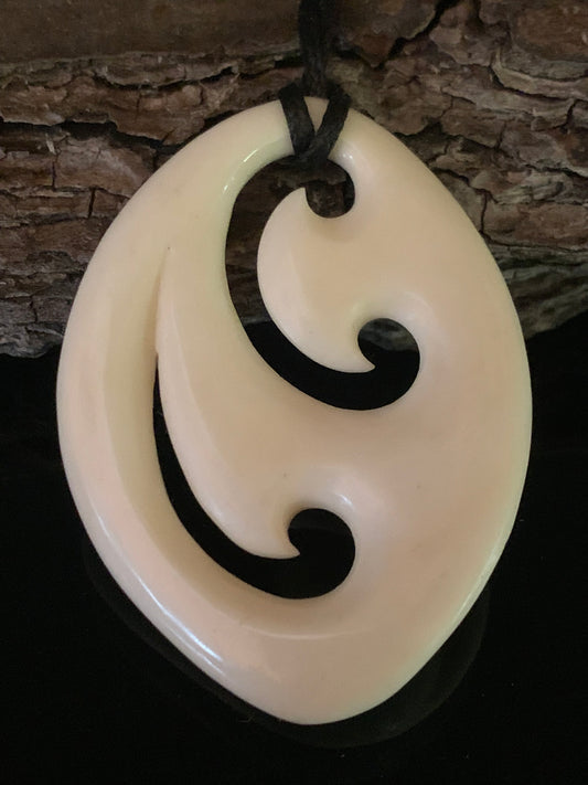 A bone pendant with Maori symbols, hanging on a waxed nylon cord against a wooden background.
