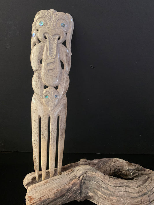 A hand-carved whale bone comb with intricate designs and decorative elements, displayed on a wooden stand against a black background.