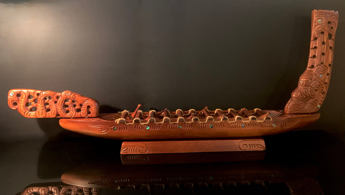 An intricately carved wooden Maori canoe sculpture with detailed carving and small green and blue paua accents