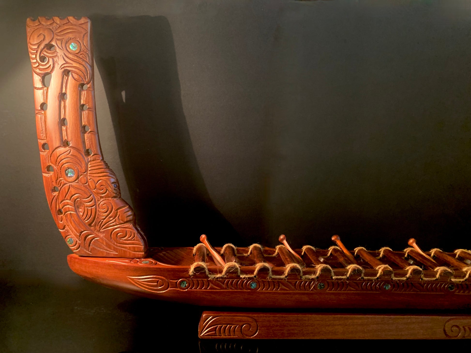 An ornate carved wooden Maori canoe hull section with intricate carvings and small tpaua shell inlays