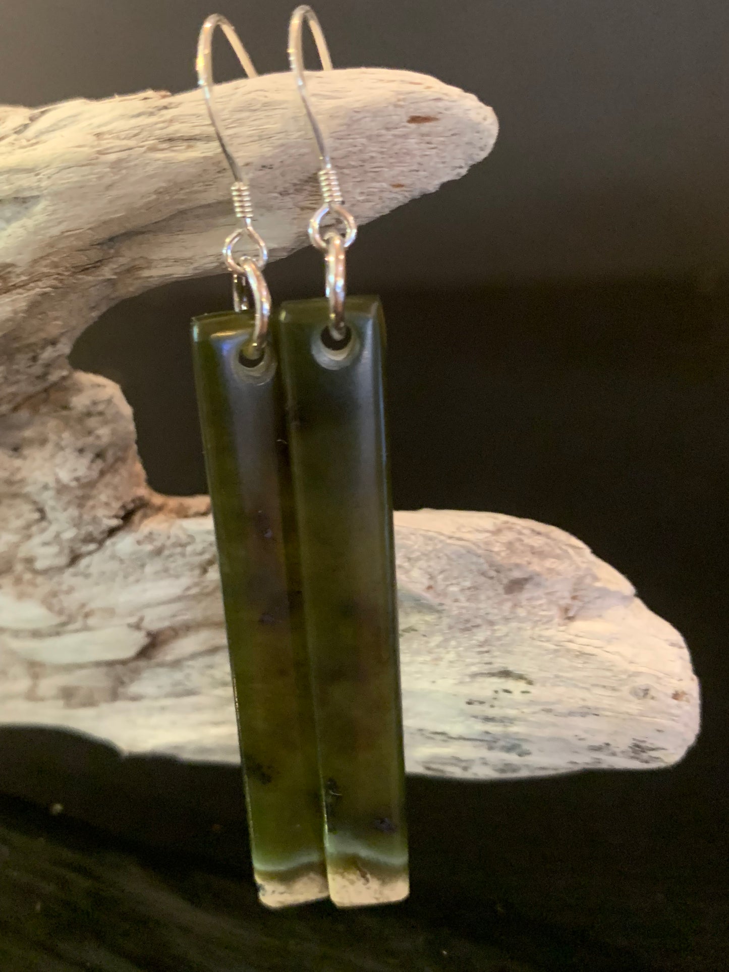 Green jade long earrings on a wooden stand
