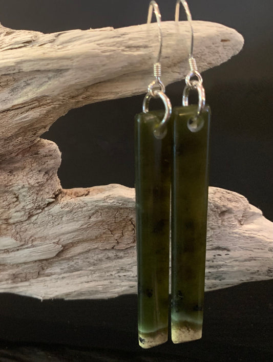 Pounamu earrings hanging from a driftwood display