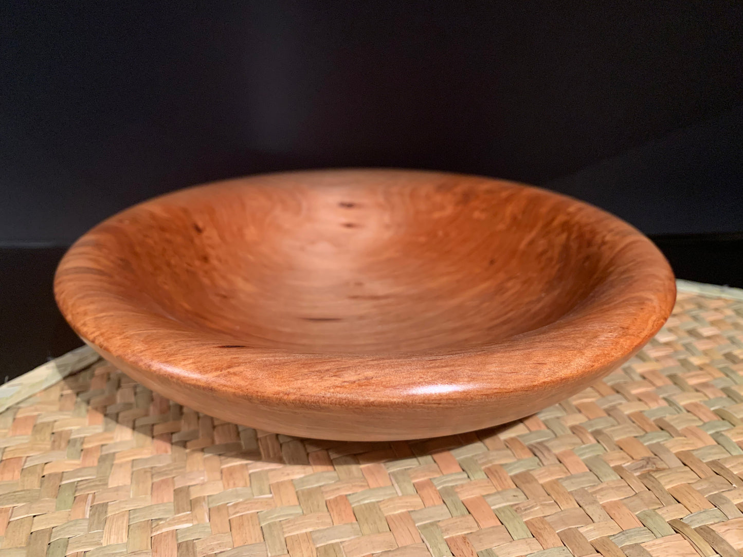 Wooden bowl displayed on a woven mat with a dark background