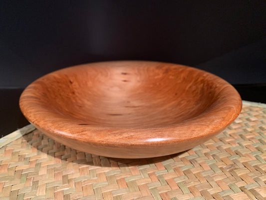 Wooden bowl displayed on a woven mat with a dark background