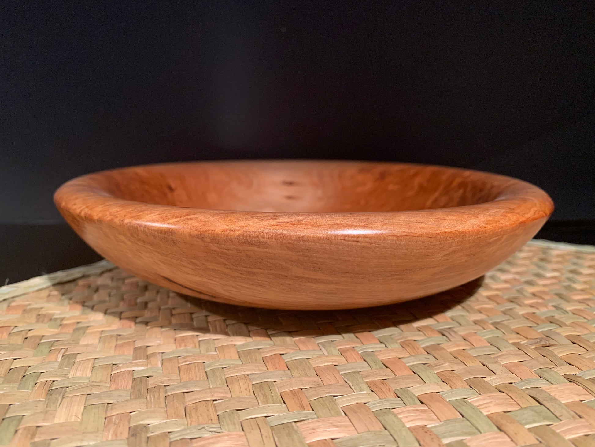 New Zealand totara wood  bowl on a woven mat with a dark background