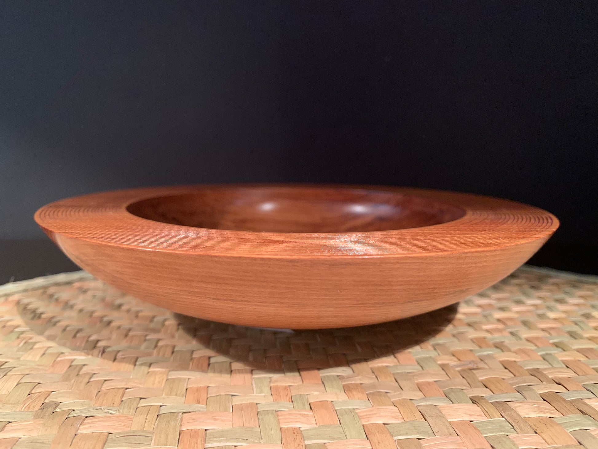 Wooden handcrafted bowl on a woven mat with a dark background.