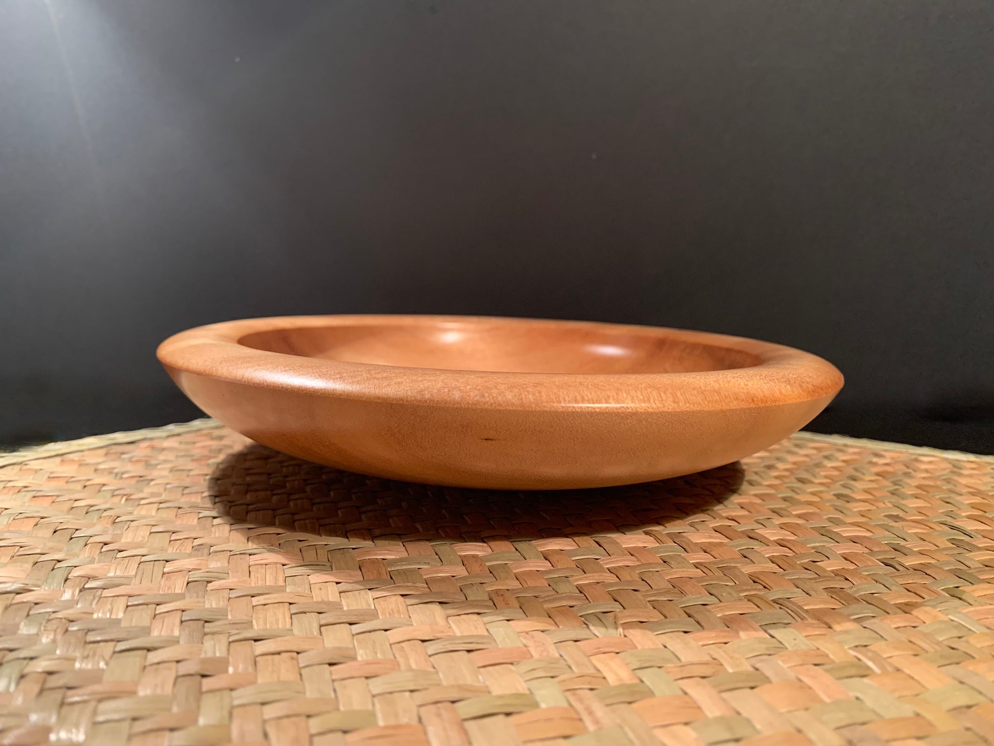 Woodturned bowl on a woven surface with a dark background.