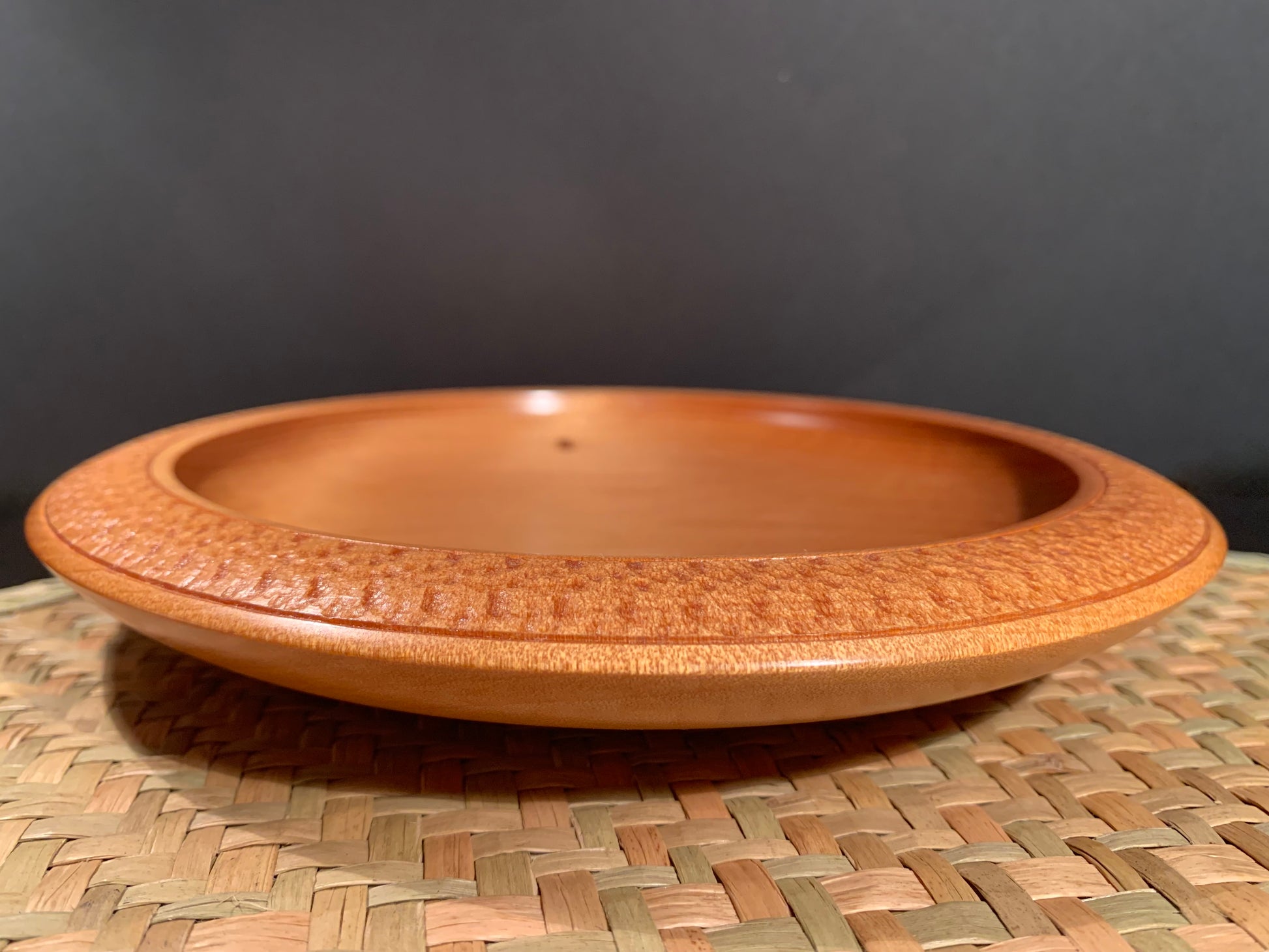 side view of wooden plate with intricate detail on rim.