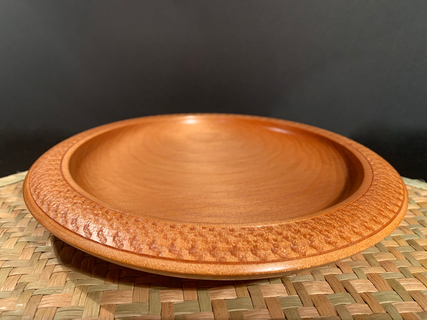 Wooden bowl with patterned edging sitting on on a woven mat.