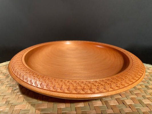 Wooden bowl sitting on on a woven mat with a dark background