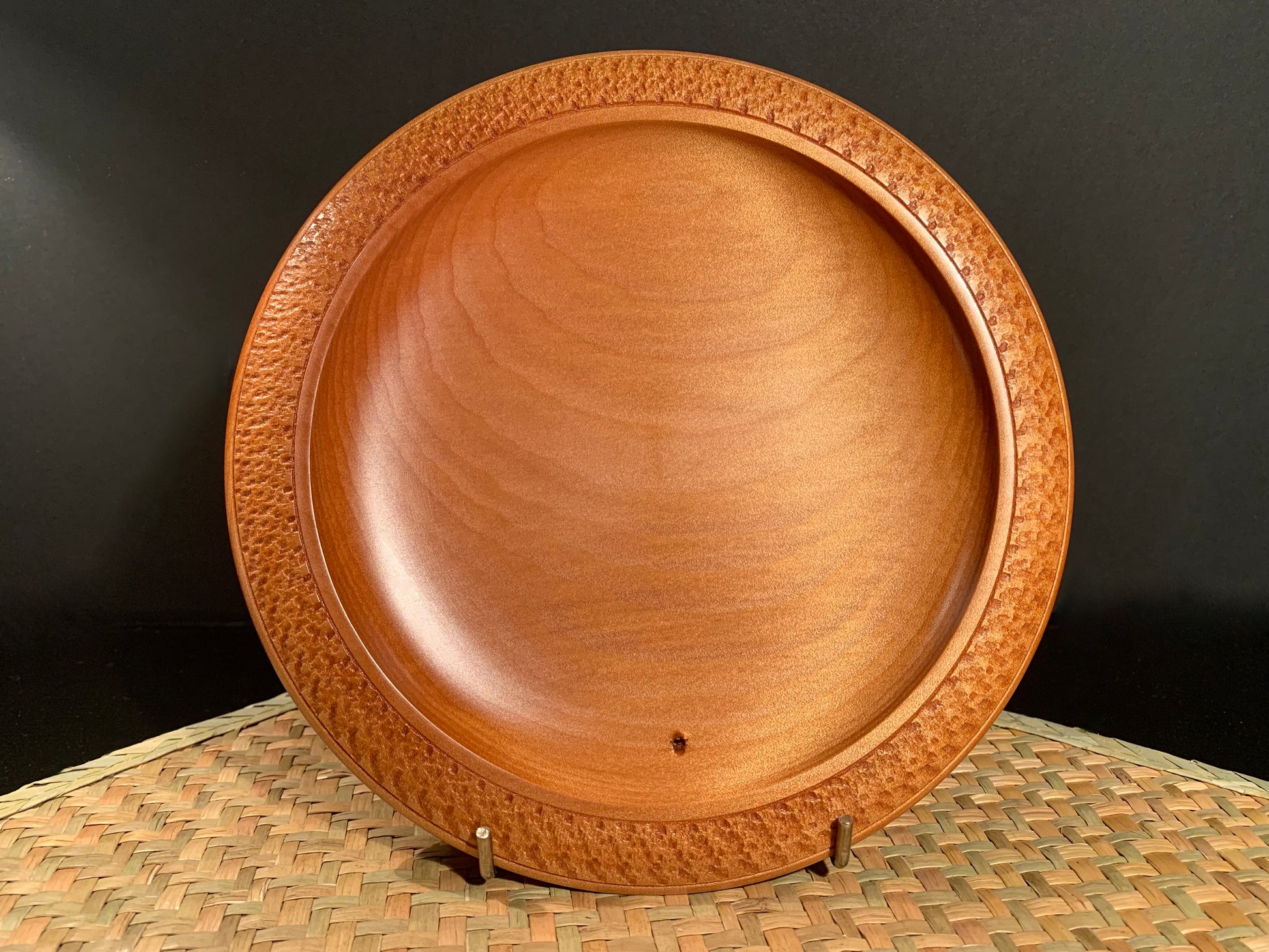 Wooden bowl with intricate rim detail on a woven surface.