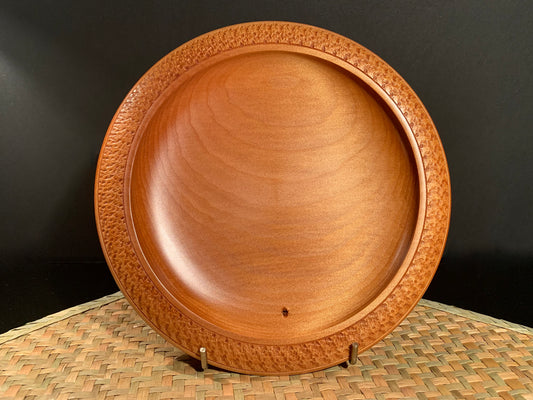 Wooden bowl with intricate rim detail on a woven surface against a black background