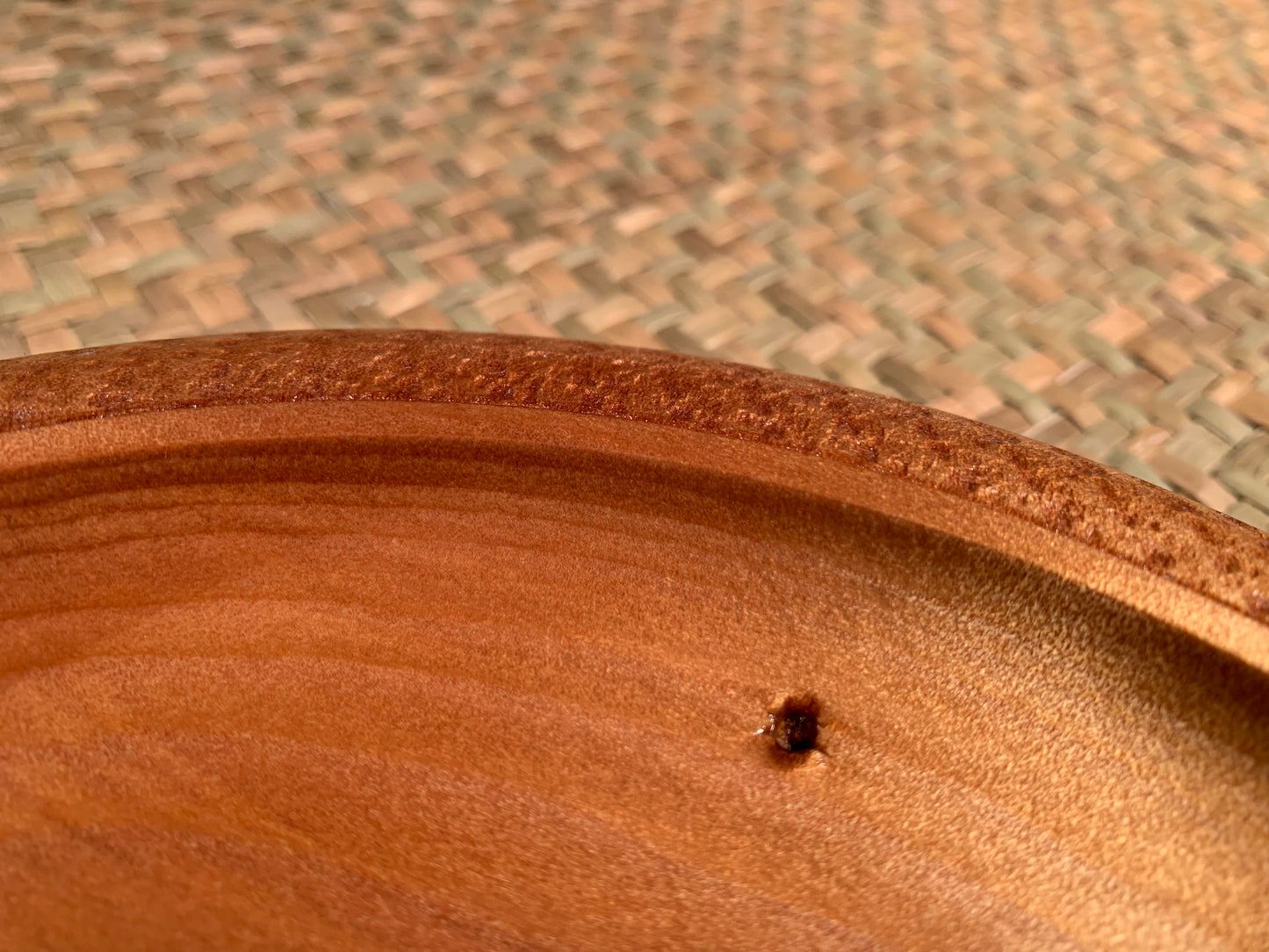 Close-up of the wooden surface of a bowl showing feature nail hole. 
