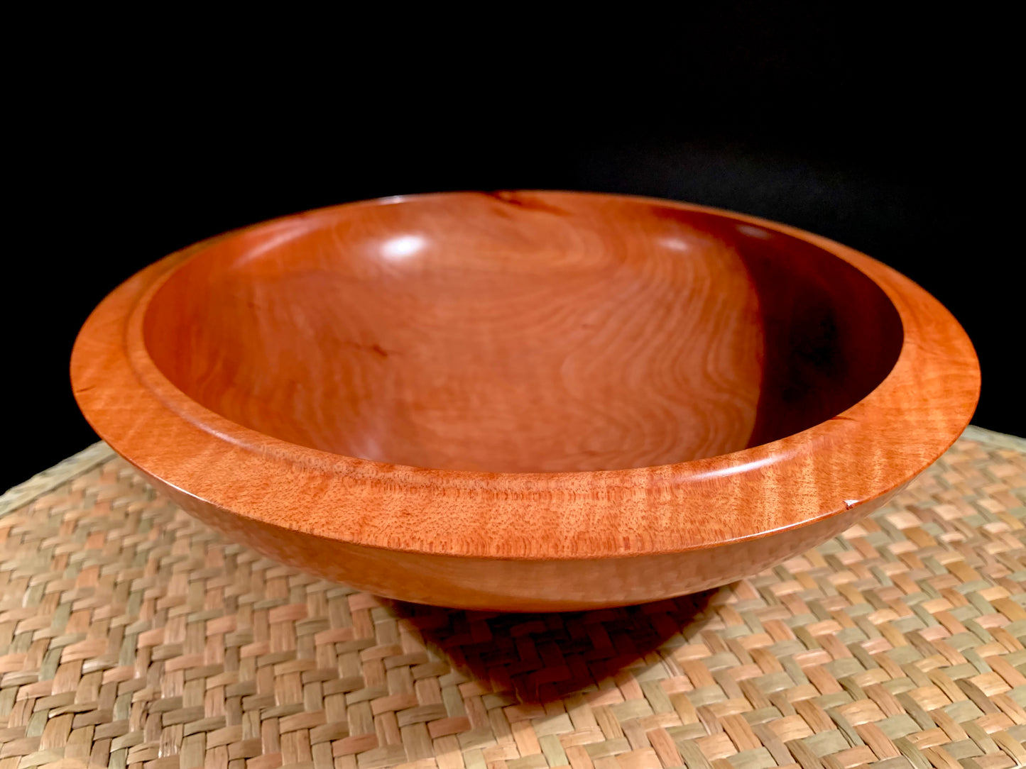 Wooden bowl with grain detailing and raised rim detail on a woven mat. 