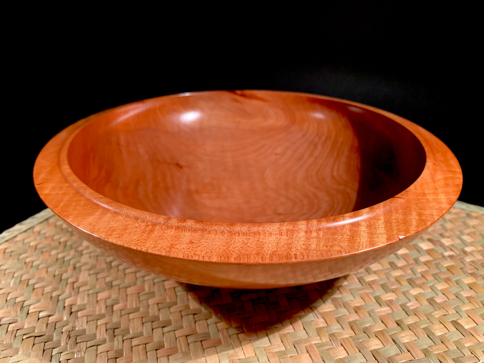 Wooden bowl with grain detailing and raised rim detail on a woven mat. 