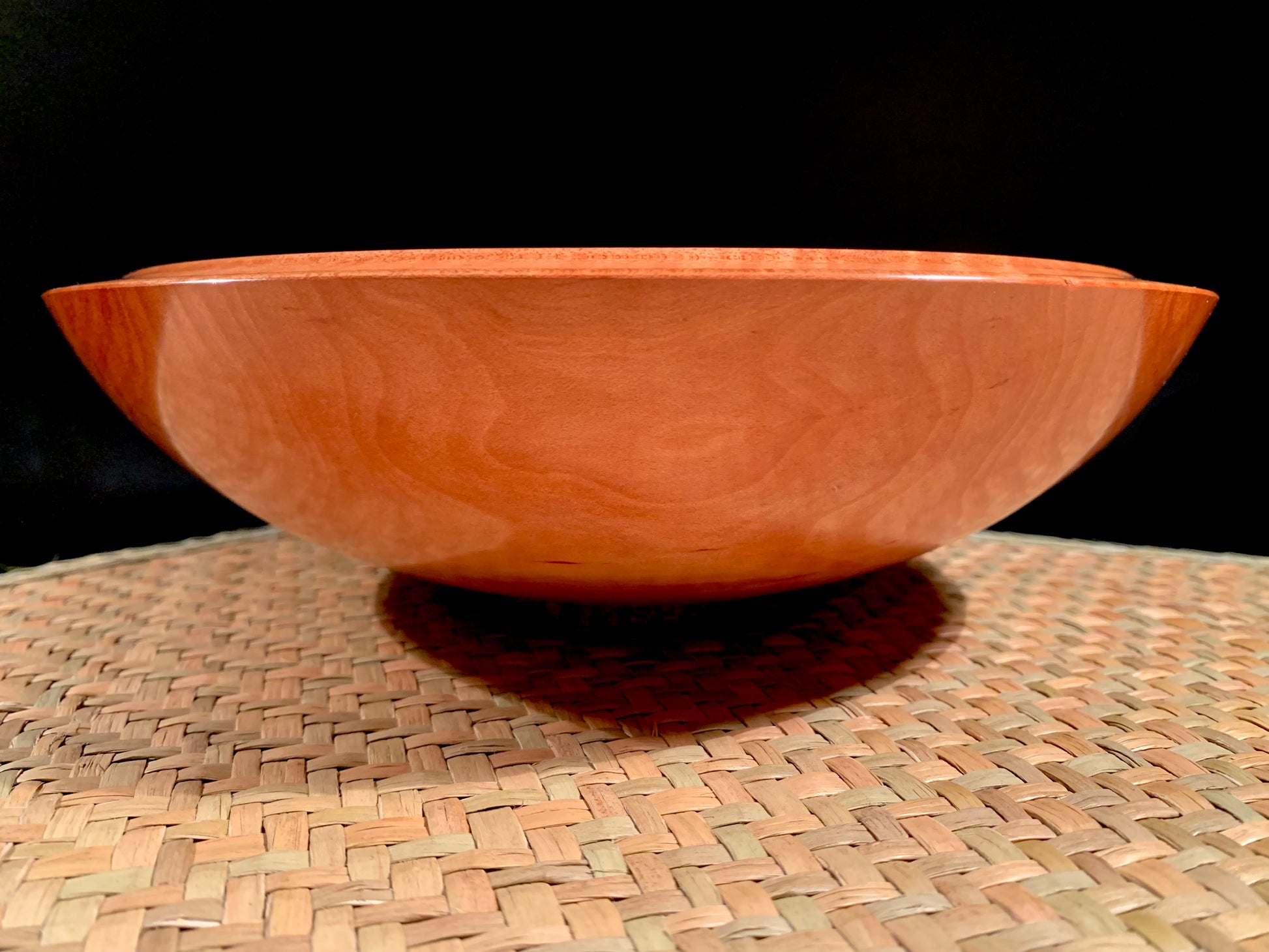 Woodturned bowl on a woven mat with a black background.