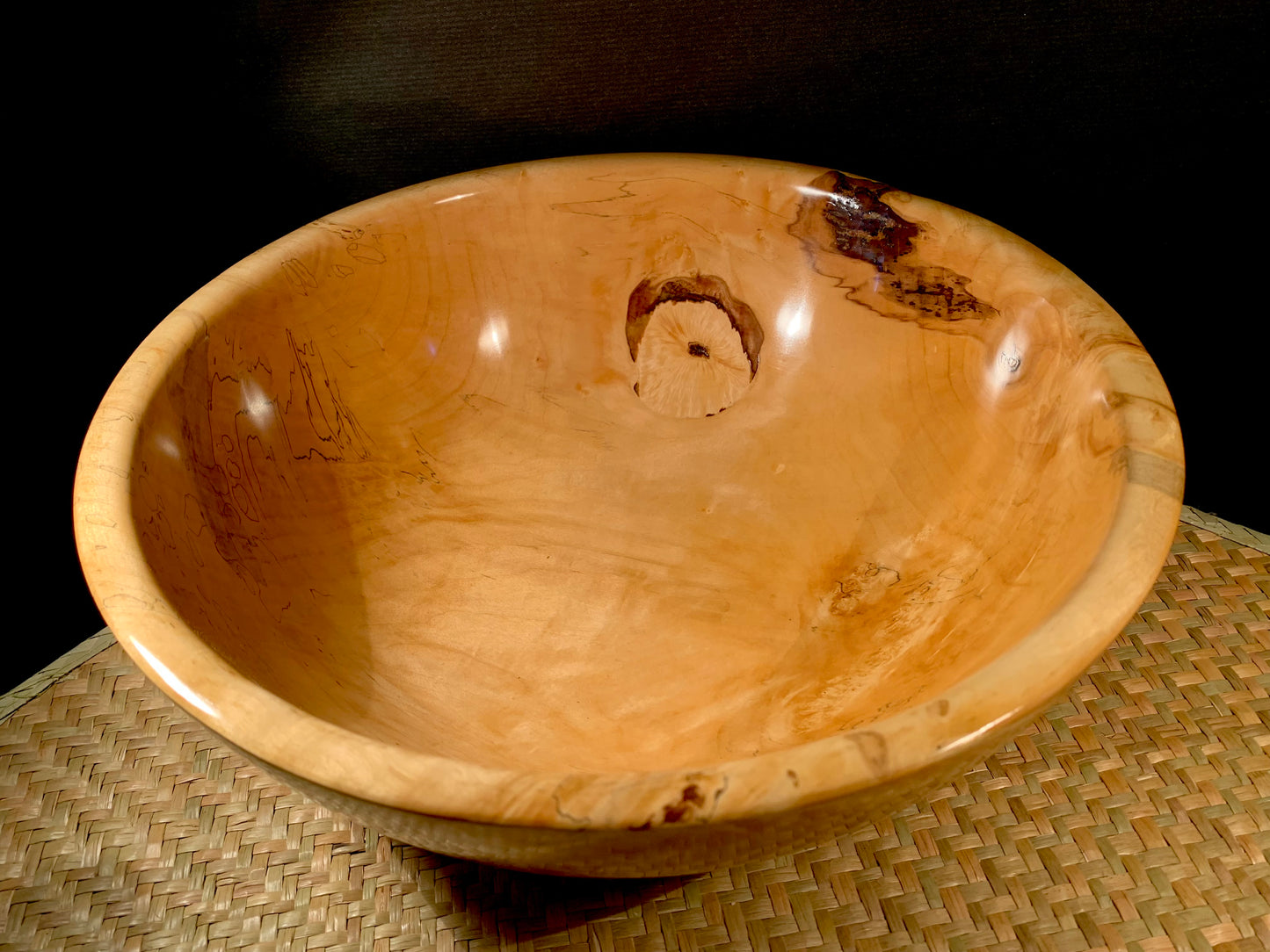 Turned wooden bowl with knot feature on a woven surface.